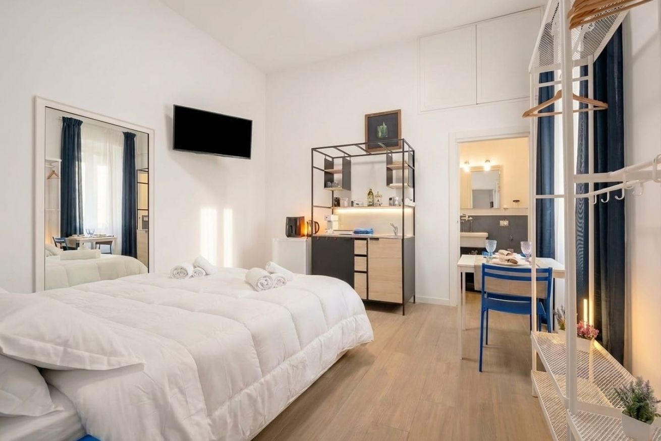 Habitación de hotel con cama, escritorio, espejo, televisión y kitchenette.