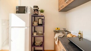 Una cucina compatta con un frigorifero bianco, una macchina per il caffè, uno scaffale con stoviglie, un lavello e un piano di lavoro con pane e una bottiglia.