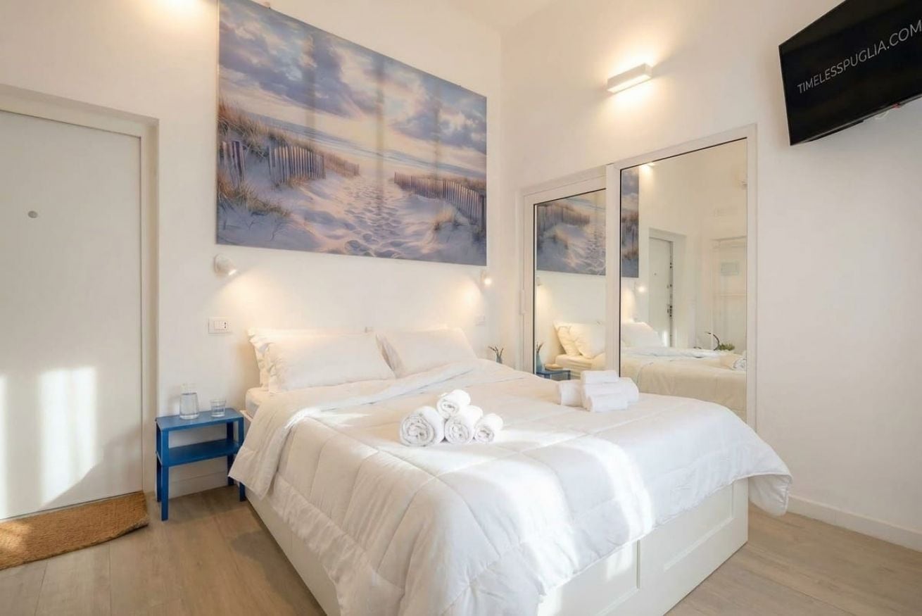 A bedroom with a bed, a bedside table, a wall-mounted TV, and a large mirror.