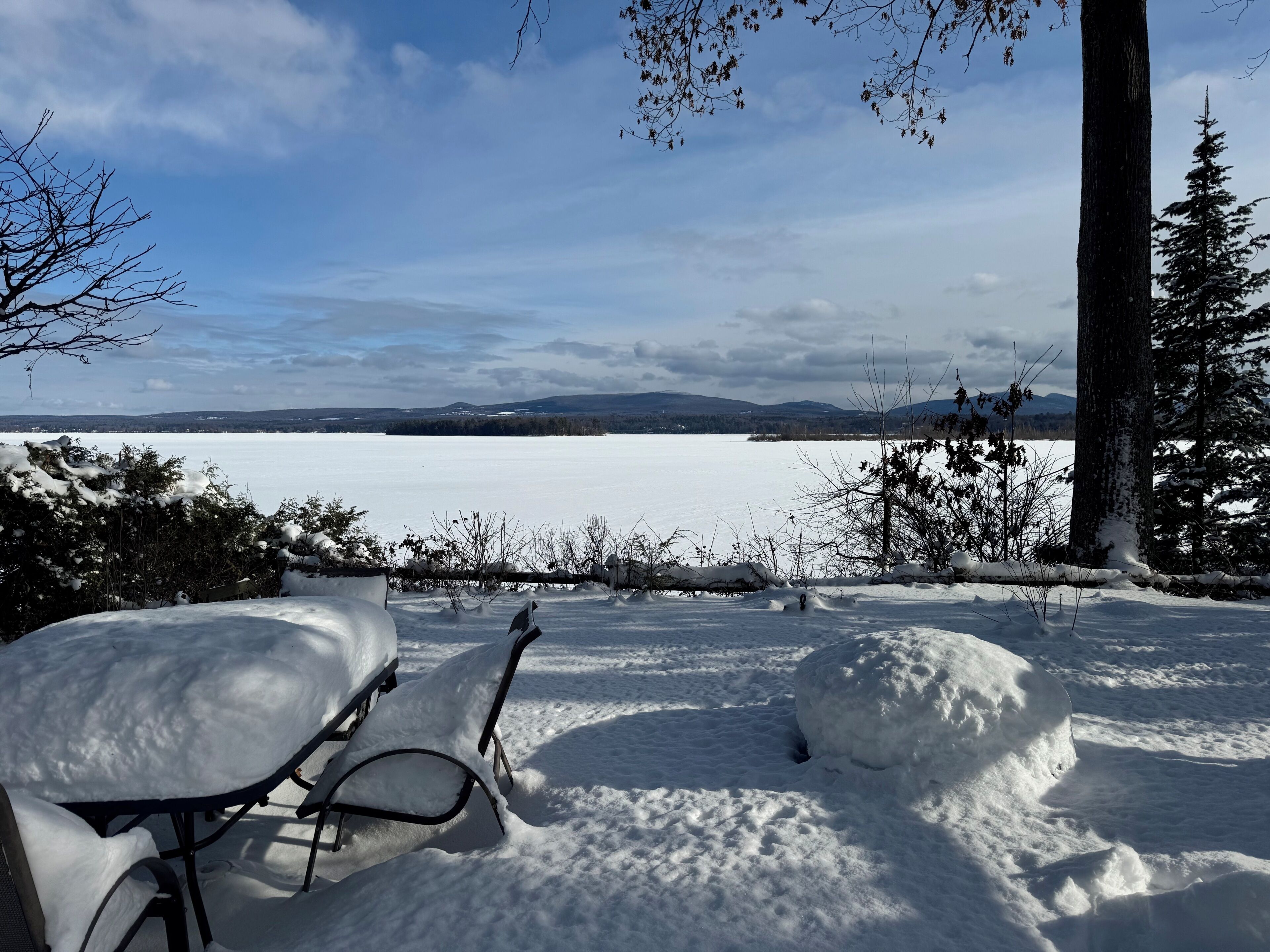 A snow-covered outdoor seating area with a view of a lake and mountains in the distance.