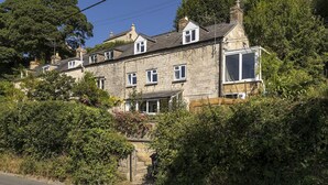 A stone house with multiple windows, a visible chimney, and a garden area with dense foliage. - Claire's Cottage -  beautiful dog friendly cottage (Brimscombe)