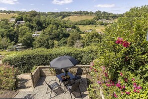 Eine Terrasse im Freien mit Tisch und Stühlen, umgeben von viel Grün und blühenden Pflanzen.