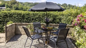 An outdoor dining area with a table and chairs, an umbrella, and a vase of flowers. - Claire's Cottage -  beautiful dog friendly cottage (Brimscombe)