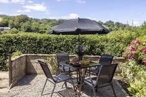 Ein Essbereich im Freien mit Tisch, Stühlen, einem Sonnenschirm und einem Blumenstrauß.