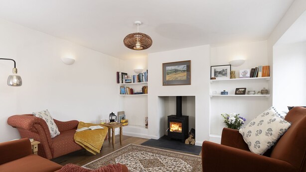 A cozy living room with a fireplace, a sofa, a coffee table, and a bookshelf. - Claire's Cottage -  beautiful dog friendly cottage (Brimscombe)