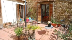 A courtyard with a stone wall, potted plants, a metal table, and a chair. - Large 4-bedroom apartment (Firenze)