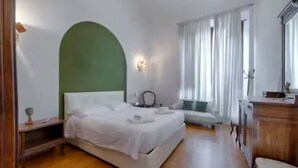 A bedroom with a bed, bedside table, lamp, and a window with curtains. - Large 4-bedroom apartment (Firenze)