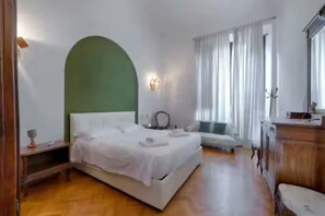 Ein Schlafzimmer mit einem Bett, einem Nachttisch, einer Lampe und einem Fenster mit Vorhängen.