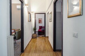 Ein Flur mit Holzboden, einem Heizkörper und einer Tür zu einem Raum mit einem roten Sofa und einer Pflanze.