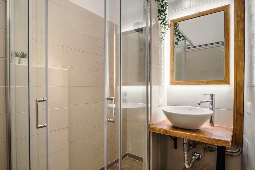 Een moderne badkamer met een glazen douchecabine, een houten wastafelmeubel met een witte wasbak en een spiegel met houten lijst.