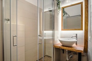 Un bagno moderno con box doccia in vetro, un mobile bagno in legno con lavandino bianco e uno specchio con cornice in legno.