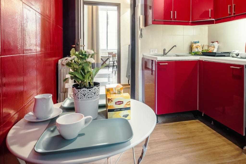 A modern kitchen with red cabinets, a white countertop, and a dining area visible in the background.