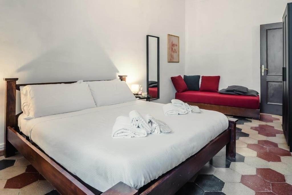 Ein Hotelzimmer mit einem großen Bett, einem roten Sofa, einem Spiegel und einer Tür.