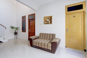 Ein Zimmer mit einer Couch, einer Tür, einer Treppe und einem Blumentopf.