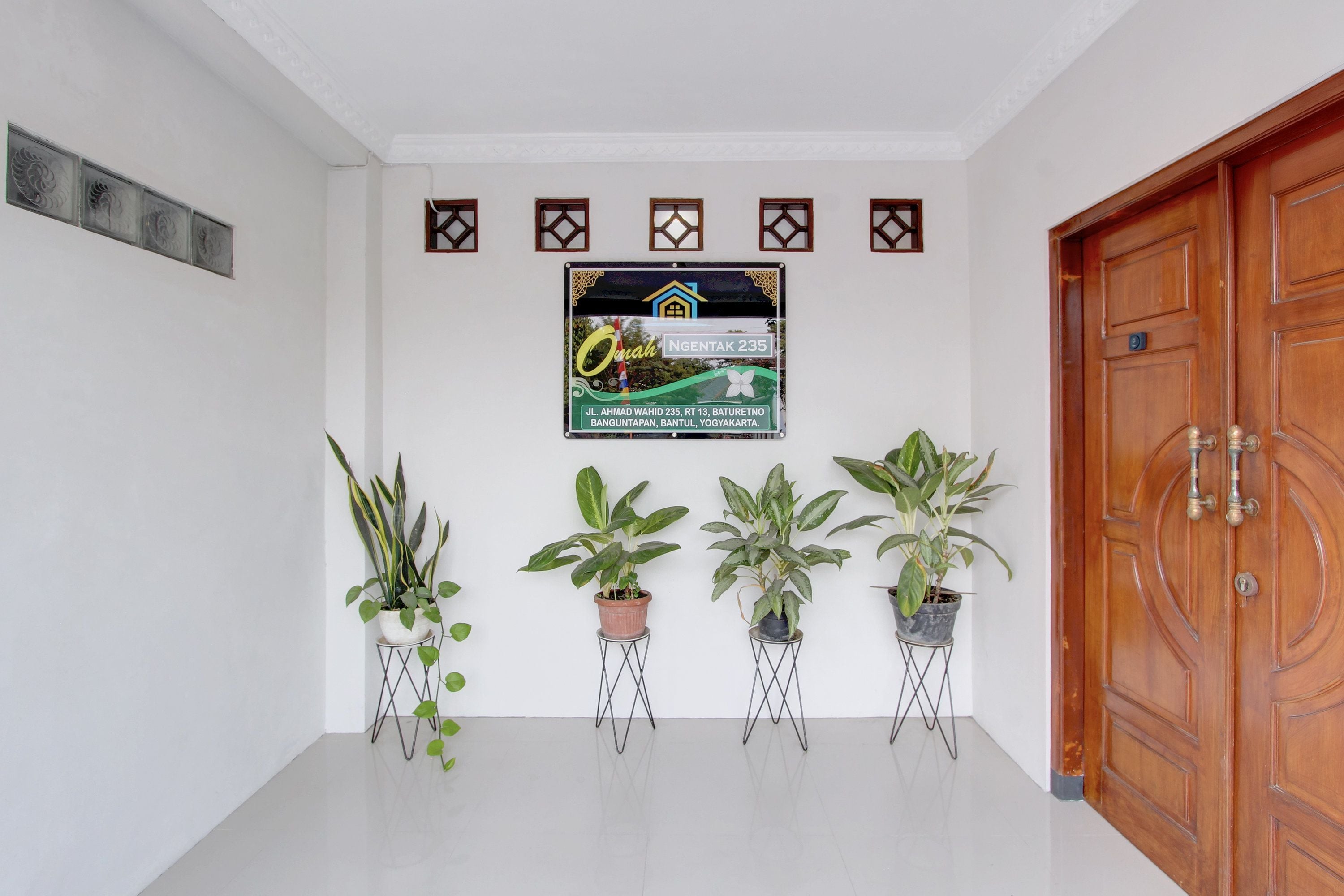 Un pasillo limpio y moderno con una puerta de madera, un letrero en la pared y cuatro macetas con plantas.