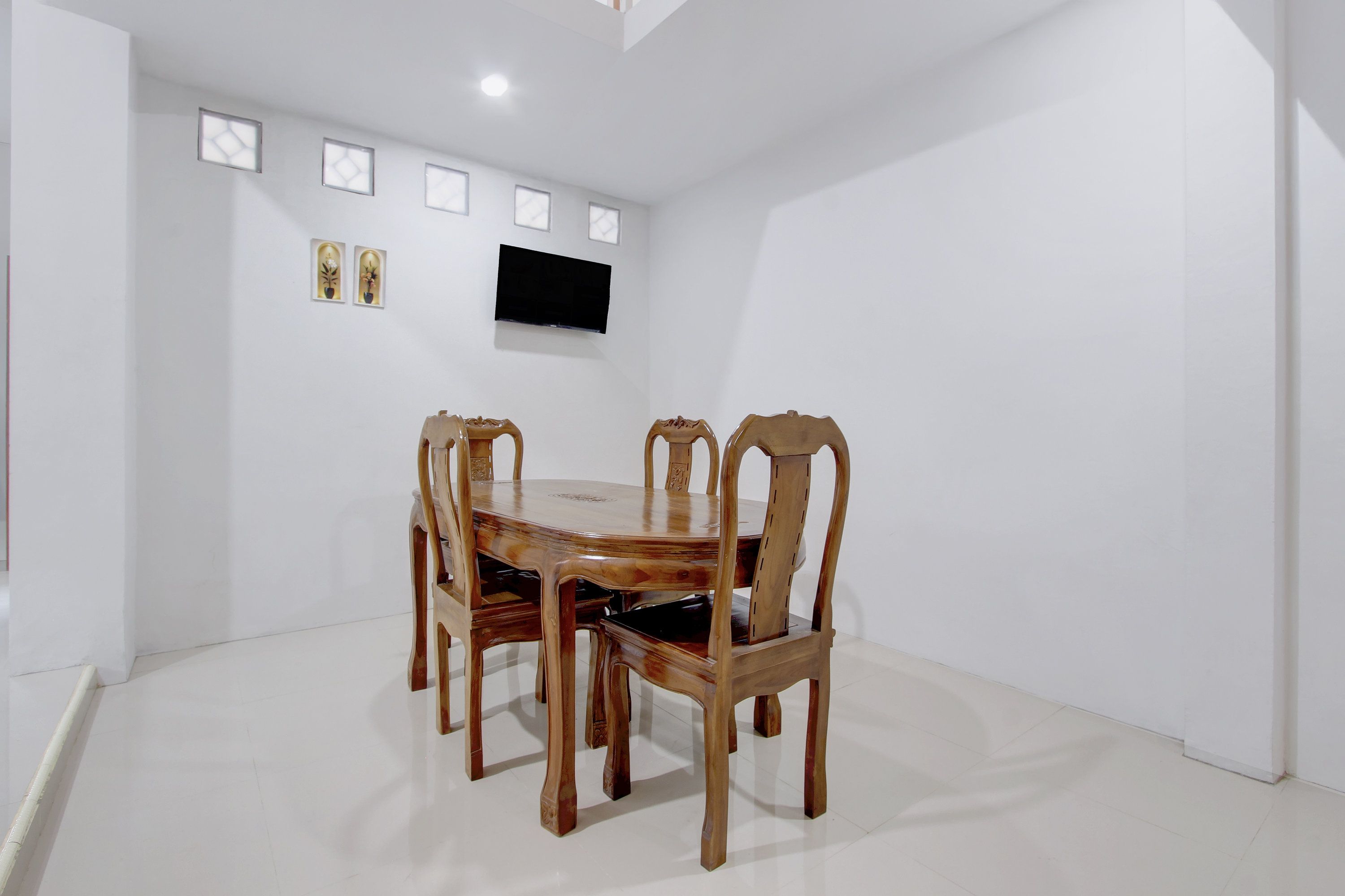 Un comedor con una mesa redonda de madera y sillas, un televisor de pantalla plana en la pared, y piso blanco.