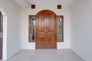 Una amplia puerta doble de madera con un espejo a cada lado, ubicada en un espacio con paredes blancas y piso de baldosas.