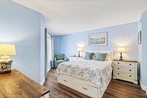 A bedroom with a bed, two bedside tables, a chair, a wooden nightstand, and a picture on the wall. - Ocean Oriented Oasis!  Indoor Heated Pool!  Pickleball! Hot Tub! (Hilton Head)