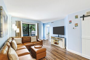 Ein Wohnzimmer mit einer Eckcouch, einem Flachbildfernseher und einem Holzboden.