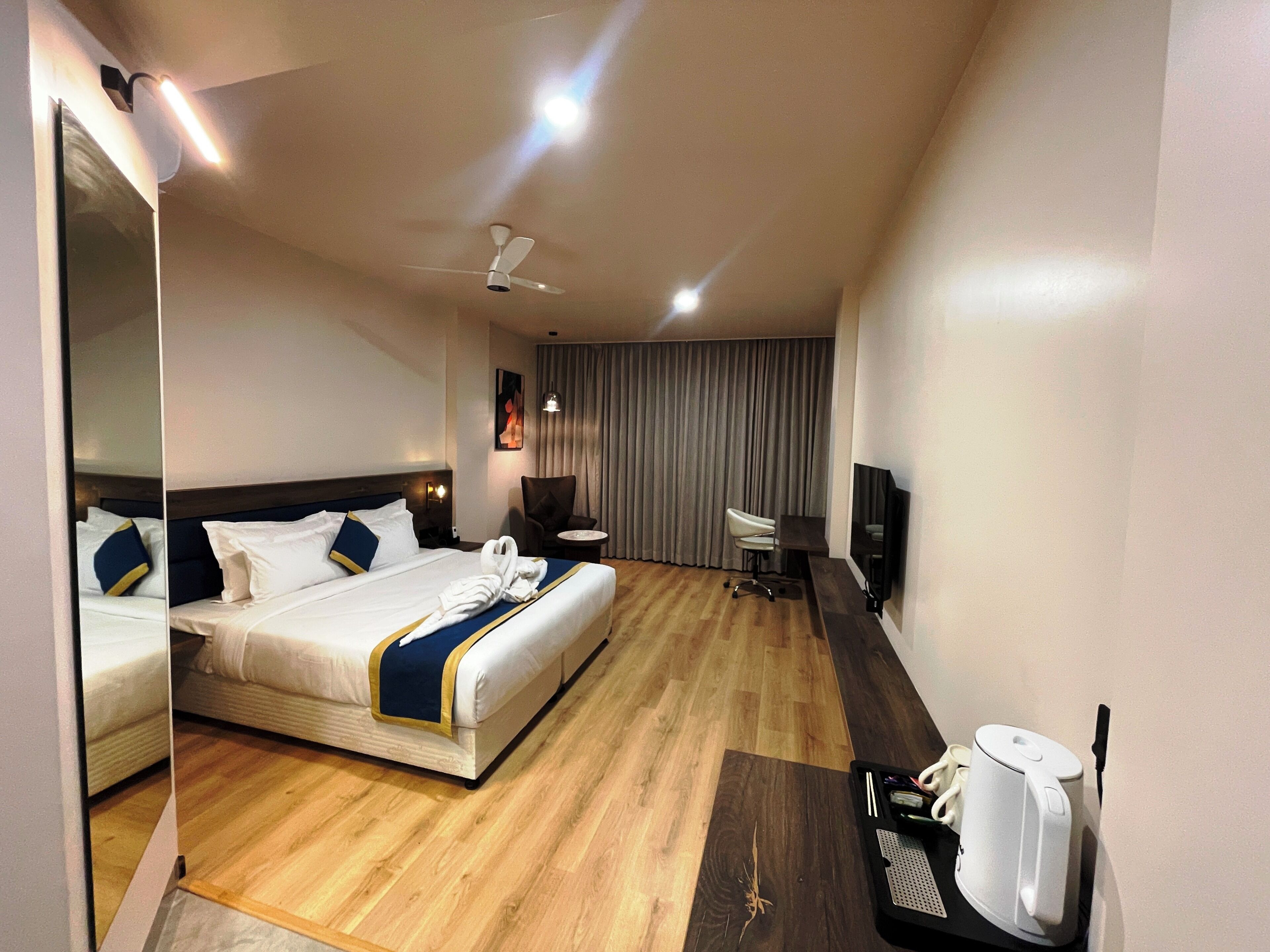 A hotel room with a bed, a desk, a chair, a TV, and a ceiling fan.