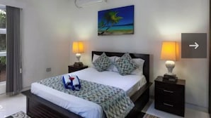 Habitación de hotel con una cama, dos lámparas de noche, un cuadro con una escena de playa y un ventanal con cortinas.