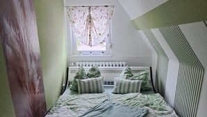 Et soveværelse med en seng, et vindue med gardiner, en radiator og en væg med et struktureret mønster.