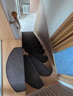 Eine Holztreppe mit schwarzem Teppich, die zu einem Raum mit einem weißen Heizkörper und einem Fenster mit Jalousien führt.