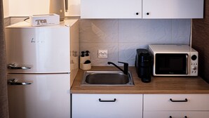 Cozinha compacta com geladeira, cafeteira, micro-ondas e pia.