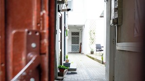 Um corredor interno que leva a uma porta, com um vaso de planta e uma cadeira à vista.