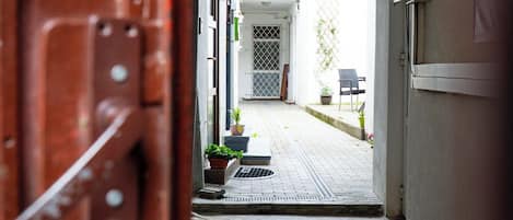 Un pasillo interior que conduce a una puerta, con una planta en maceta y una silla visibles afuera.