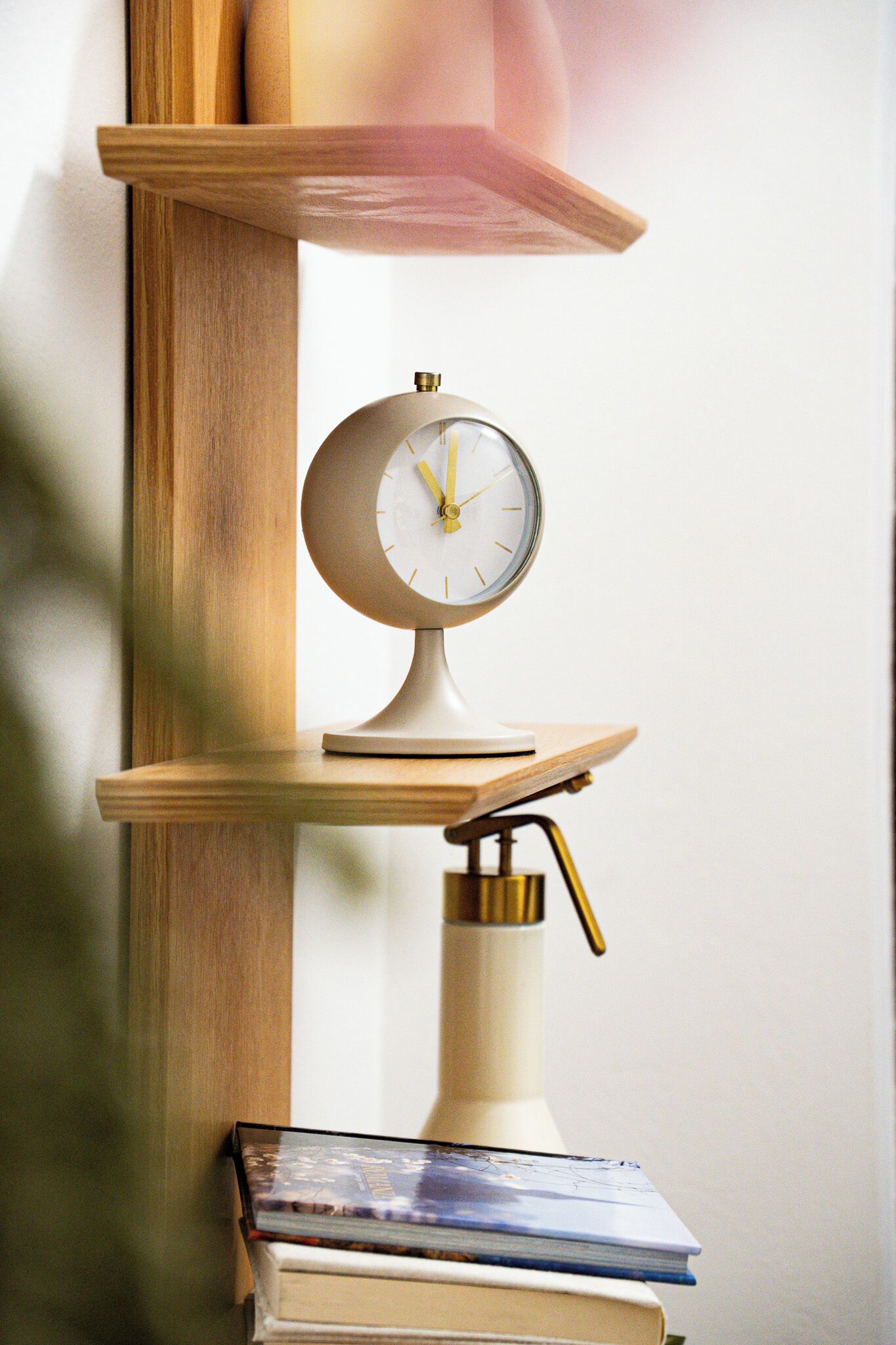 A wall-mounted clock with a classic design, positioned above a stack of books on a wooden shelf.