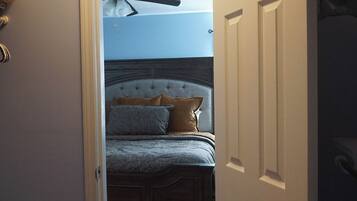 Ein Schlafzimmer mit Bett, Deckenventilator und einer Tür zu einem weiteren Raum.