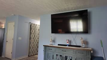 Quarto com televisão de tela plana na parede, porta estampada e armário azul com objetos decorativos.