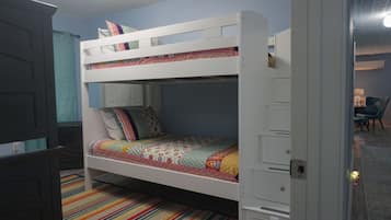 A bunk bed with a colorful quilt, a striped rug, and a door to another room.