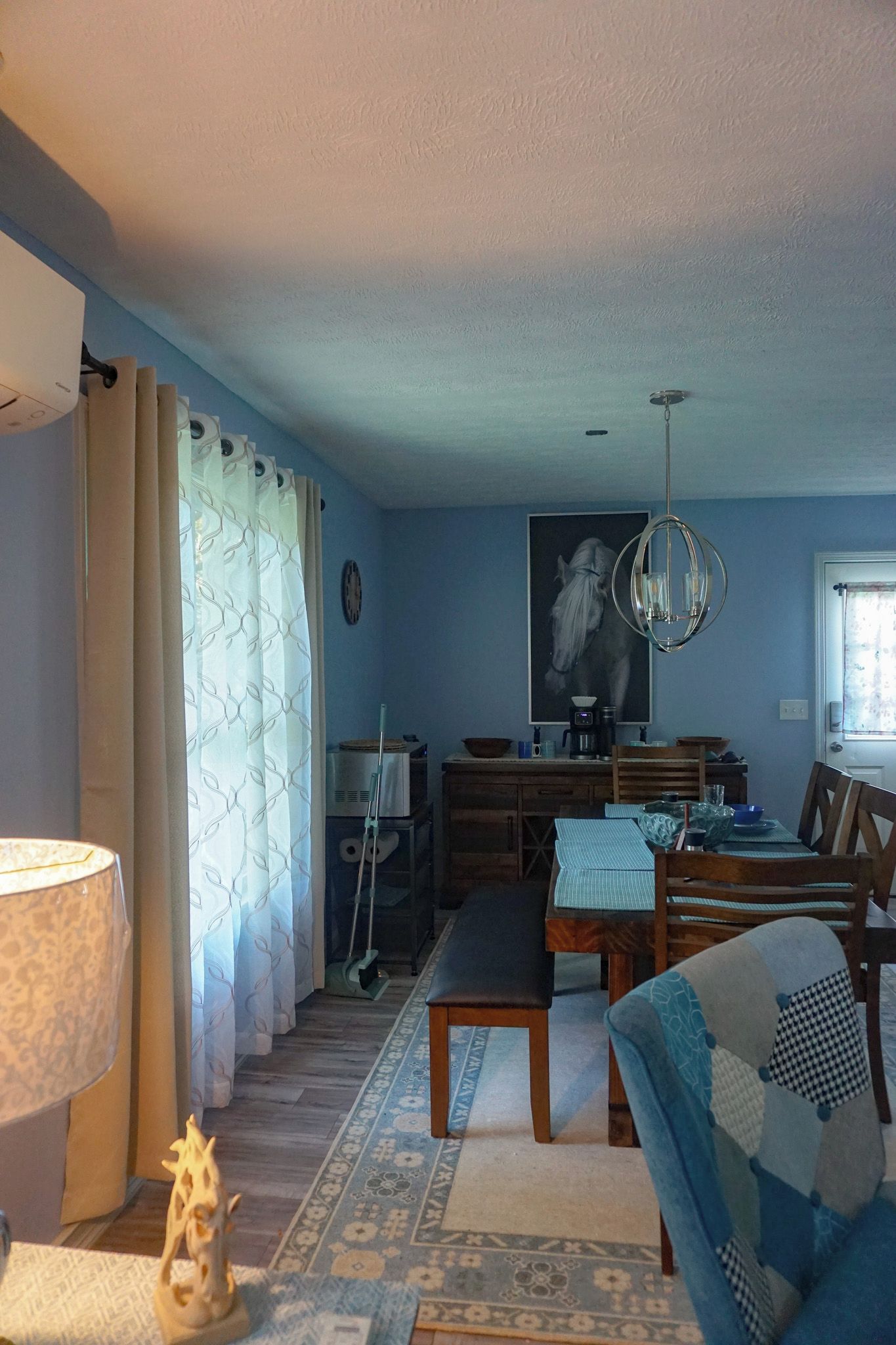 A dining area with a table set for four, a chandelier, and a painting on the wall.