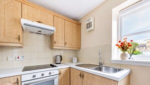 Una cocina compacta con armarios de madera, horno empotrado, estufa, lavabo y ventana con flores.