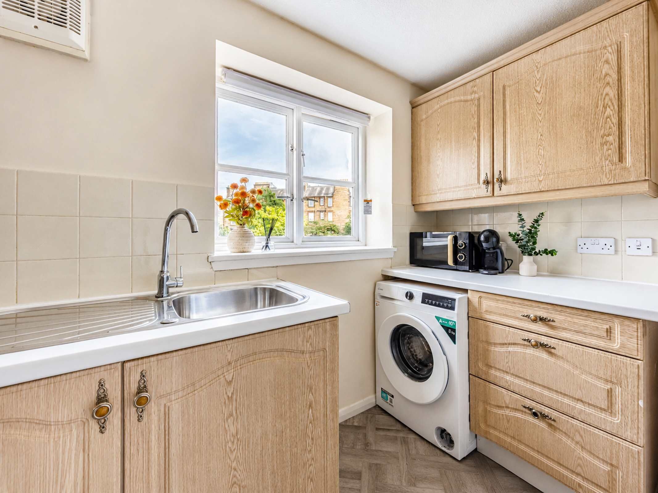 A kitchen with a built-in washing machine, a window with flowers, and wooden cabinets.