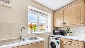 Una cocina con lavadora integrada, una ventana con flores y armarios de madera.