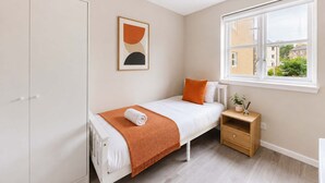 Un dormitorio con cama, mesita de noche, armario, ventana con vistas y un cuadro en la pared.