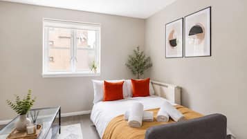 A hotel room with a bed, a bedside table with a vase and candles, a window, and two framed pictures on the wall.