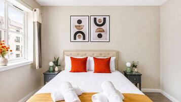 A hotel room with a large bed, two nightstands, a window with curtains, and two wall art pieces.