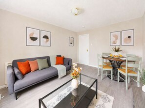 A living room with a grey sofa, a glass coffee table, and a dining area with a wooden table and chairs. - Charming 2BR Flat Near Holyrood Park & Old Town (Edinburgh)