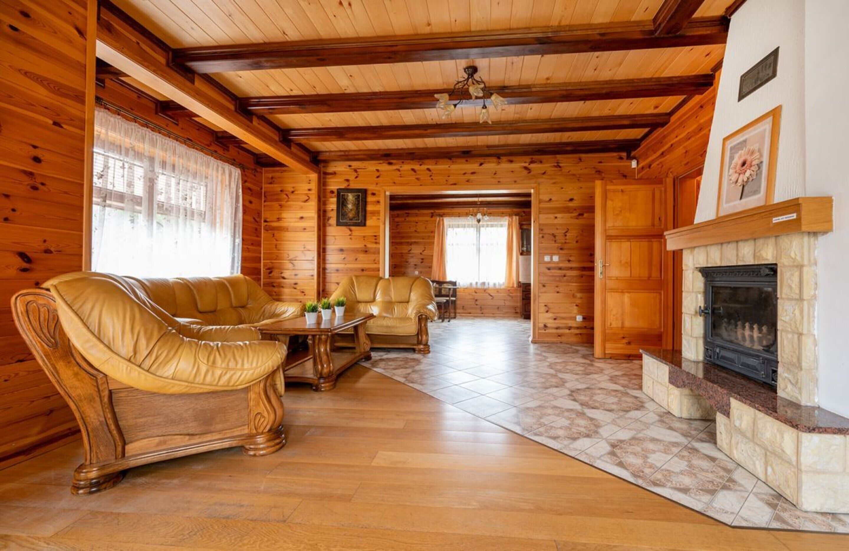 A log cabin interior with a fireplace, leather sofas, and a dining area.