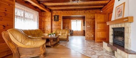 Interior de cabana de madeira com lareira, sofás de couro e área de jantar.