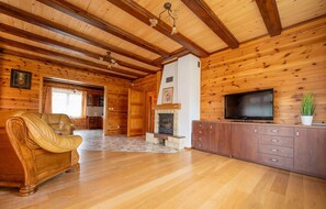 Ein rustikaler Blockhaushof mit Ledersofa, Kamin, Fernseher und Holzwänden.