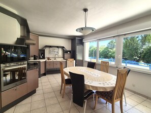 A kitchen with a dining area, a built-in oven, and a window with a view of greenery. - Pet-friendly Country House in Central Brittany (Saint-Vran)