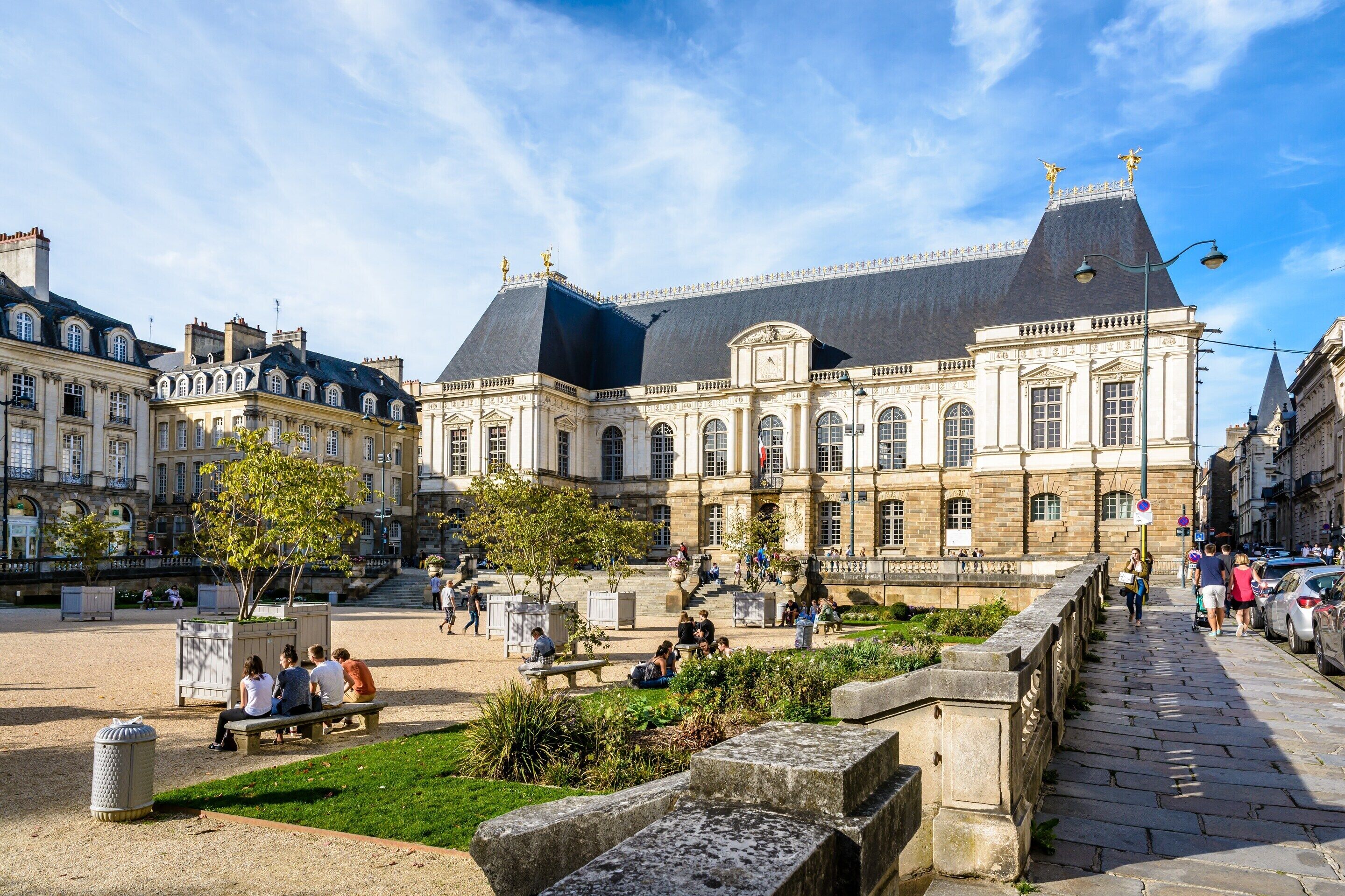 A historic building with classical architecture, a courtyard with seating, and a pedestrian bridge.
