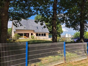 A residential house with a fenced yard, a covered porch, and a large tree in the foreground. - Pet-friendly Country House in Central Brittany (Saint-Vran)