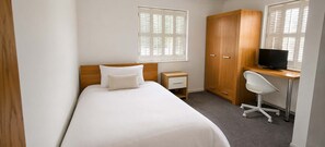 Une chambre à coucher comprenant un lit, un bureau avec une chaise, une armoire et un téléviseur.