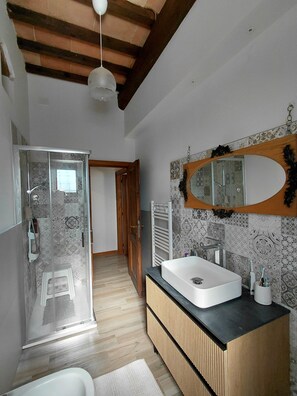 Een moderne badkamer met een glazen douchecabine, een grote spiegel en een houten wastafelmeubel.